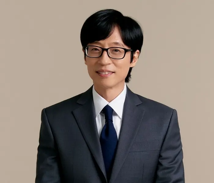 刘在石身穿正装微笑着,背景模糊,展现出国民MC的自信与亲和力,预示着他在2026年综艺界的新动向。