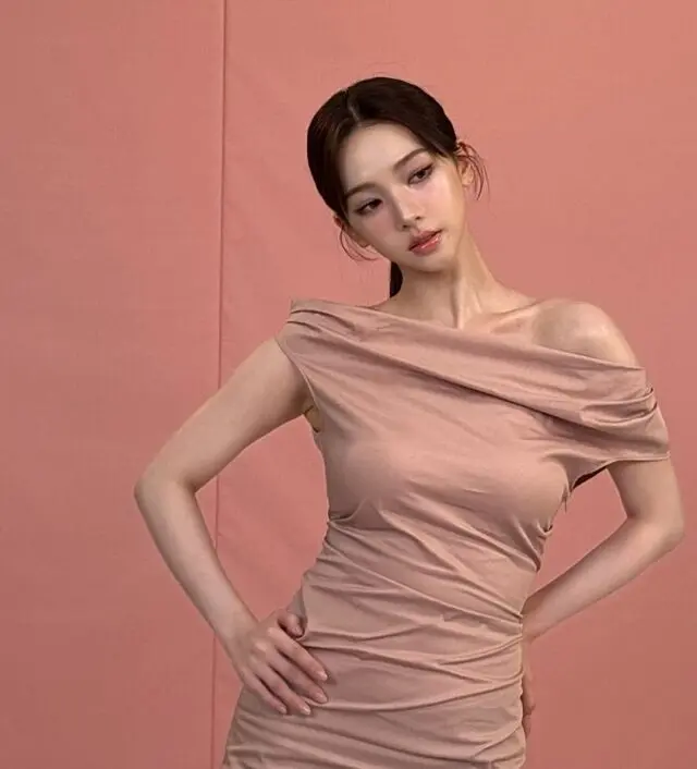 Karina身穿白色露肩礼服在粉色背景前侧身站立，展现优越的直角肩和锁骨